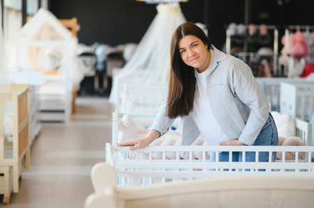 Smiling pregnant woman choosing baby crib at shopping mall.の写真素材