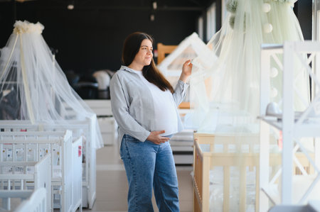 Happy pregnant woman choosing a baby crib in the store.