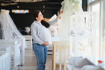 Smiling pregnant woman choosing baby crib at shopping mall.の写真素材