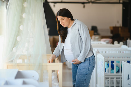 Smiling pregnant woman choosing baby crib at shopping mall.