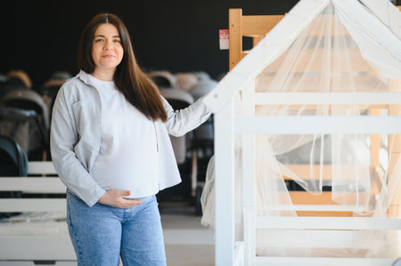 Pregnancy shopping concept. Pregnant woman choosing cradle cot or crib for newborn at baby shop...