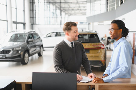 client male purchasing automobile in dealership, signing paper, with car dealer. Concept of buying new auto at showroom.の写真素材