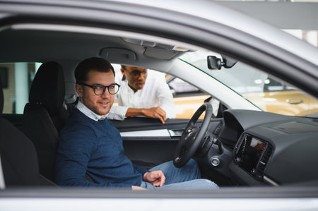 Male car dealer having conversation with pensive young man client at showroom. Man listening manager while buying car at dealership centerの写真素材