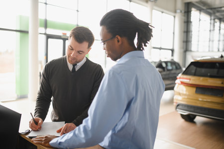 Dealer with male customer signing documents at auto salon. Bearded man in buying new vehicle at car center.の写真素材