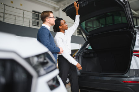 Male car dealer helps customer choose car in car dealership. Man buys new car.