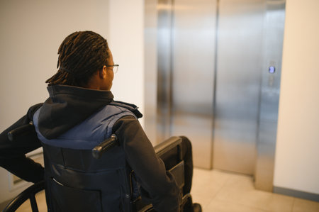 Rear view of a young African American man in a wheelchair waiting for the elevator in a modern...