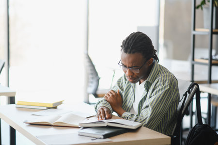 Dedicated student with books and diploma studies in a bright university library, preparing for...