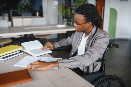 Young man with a disability reading intently in a modern library, fully engaged in his studies and...