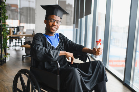 African American student in a wheelchair proudly holding a diploma, wearing a graduation cap and...