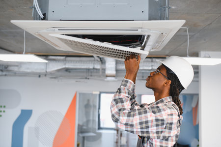Hvac technician inspecting and repairing a ceiling mounted cassette air conditioning unit, ensuring...