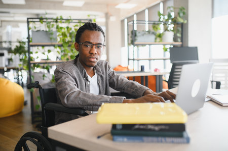 Young man in a wheelchair working on a laptop in a bright, plant filled office, showcasing...