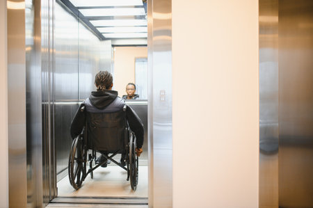 Rear view of a young African American man using a wheelchair entering a modern elevator, promoting accessibility and inclusionの写真素材