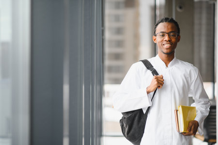 Smiling african american medical student carrying books and a backpack, standing in a university hallway, symbolizing education and achievementの写真素材