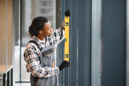 Young african american worker using a spirit level while installing a window in a modern office buildingの写真素材