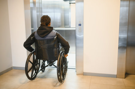 Rear view of a young black man with a disability entering a modern elevator using his wheelchair, promoting accessibility and independent mobilityの写真素材
