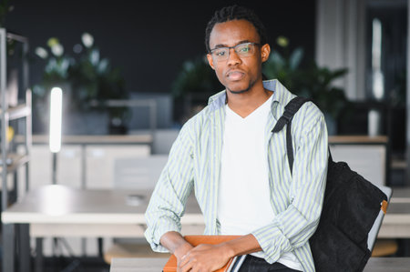 Portrait of a focused African American university student holding books and a notebook, ready for studying and academic success in a modern libraryの写真素材