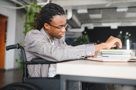 Young man with disability using a wheelchair is concentrating on his studies, highlighting the themes of inclusivity, accessibility, and determination in educationの写真素材