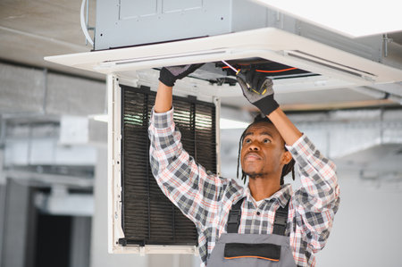 African american hvac technician repairing air conditioning ventilation system using screwdriverの写真素材