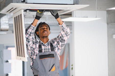 Young african american male technician repairing air conditioning ventilation system in office buildingの写真素材