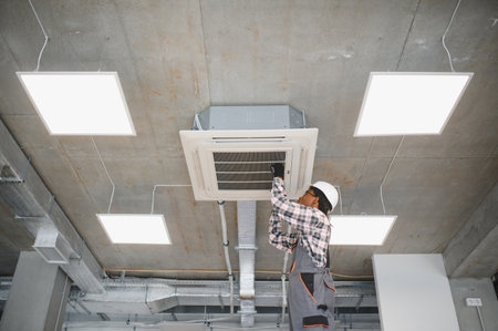 African american hvac technician repairing air conditioning unit on ceiling in industrial buildingの写真素材