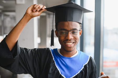 Proud graduate student is smiling and holding his graduation cap during his graduation ceremony at the universityの写真素材