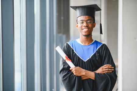 Smiling african american university student wearing graduation gown and holding diploma, celebrating academic achievementの写真素材