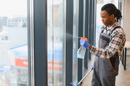 Young man cleaning windows in a modern office building, spraying detergent and skillfully using a squeegee for a spotless finishの写真素材