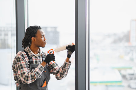 Professional worker applying sealant to a window frame using a silicone gun, ensuring airtight insulation and energy efficiencyの写真素材