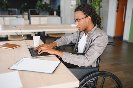 Young professional man with disability working on laptop in modern office, demonstrating inclusion...