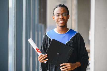 Smiling african american student in graduation attire holding diploma, symbolizing academic...