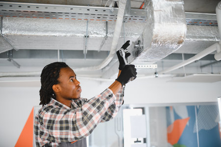 Young african american worker tightening bolts on air conditioning ductwork using a ratchet,...