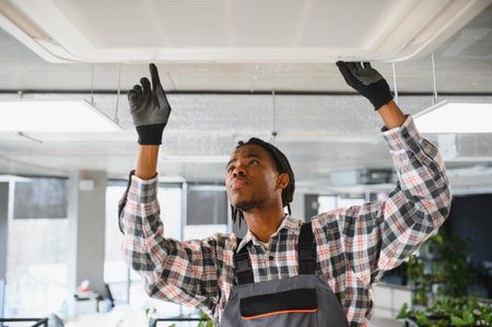 Young african american male technician inspecting and repairing an air conditioning ventilation...