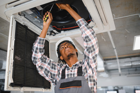 African american worker expertly repairs an air conditioning unit, ensuring efficient ventilation in a modern buildingの写真素材