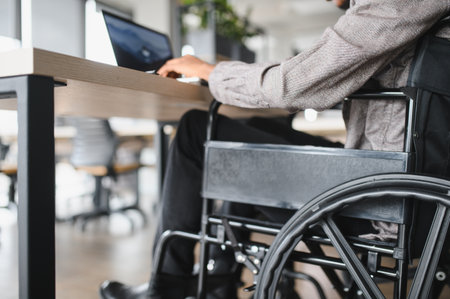 Confident young professional using laptop at desk in modern office, demonstrating integration and accessibility in workplaceの写真素材
