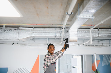 Young african american hvac technician installing an air conditioning system in a modern building, ensuring proper ventilation and climate controlの写真素材