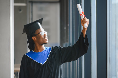 Happy student wearing graduation gown and cap proudly showing his diploma at the university