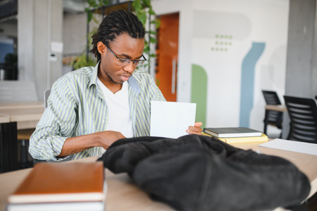 Young african american male student putting notes in backpack after studying in university library
