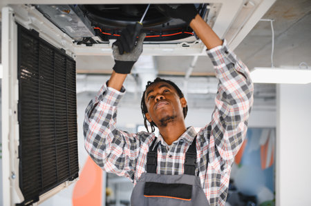 Electrician repairing a ventilation system with a screwdriver, diligently maintaining essential...