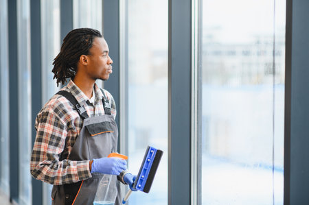 Young man cleaning windows using professional tools and products, ensuring hygiene and transparencyの写真素材