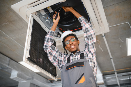 Young african american maintenance worker repairing an air conditioning system with a screwdriver,...