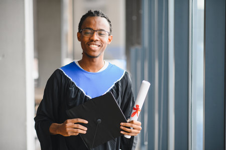 Young man smiling and holding his graduation certificate and mortarboard after graduating from universityの写真素材