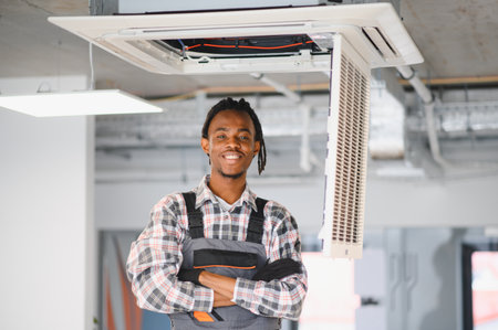 African american technician expertly repairing a ceiling mounted air conditioning unit in a modern office, ensuring optimal ventilationの写真素材