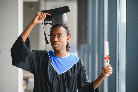 Young doctor adjusting graduation cap while proudly holding diploma, celebrating academic...