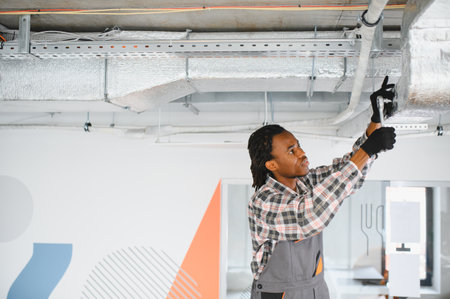 Young african american male technician using a wrench, repairing an air conditioning ventilation...