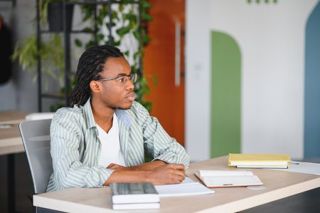 Young african american student taking notes and studying in a modern university library or coworking...