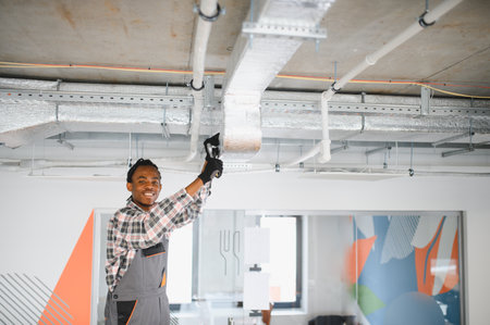 Young african american worker installing an air conditioning system in a modern office, ensuring optimal climate control and comfortの写真素材