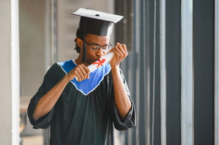 Young African American male student kissing his diploma, celebrating his graduation in a university...