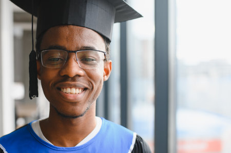 Portrait of a smiling African American student wearing graduation gown and cap, celebrating academic achievement and future careerの写真素材