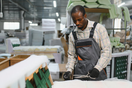 Skilled craftsman working on sofa production in a furniture factory, carefully cutting fabric with large scissorsの写真素材