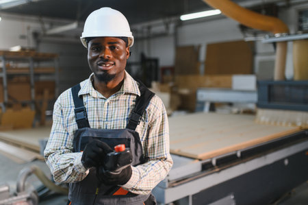 Confident african american carpenter controlling a cnc machine in a furniture factory, showcasing expertise and modern woodworking technologyの写真素材